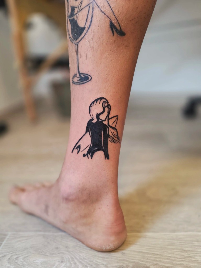 Tatouage silhouette noire d'une surfeuse à la cheville