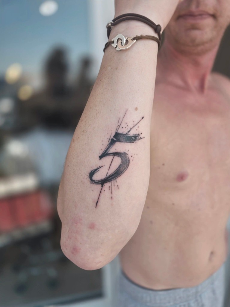 Tatouage chiffre 5 en pinceau avec éclaboussures sur l'avant-bras
