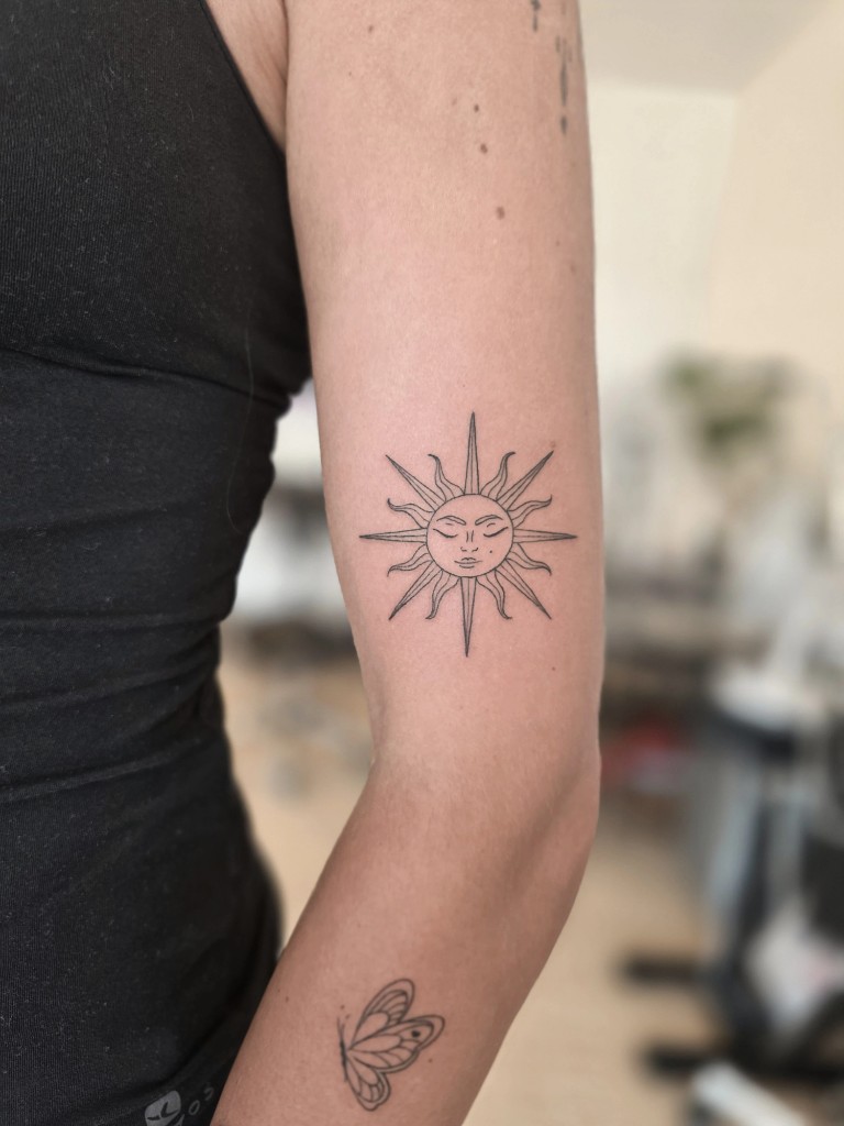 Tatouage soleil au visage fine line sur le bras